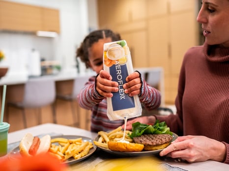 Young girl squeezing condiment out of AeroFlexx Pak onto a burger