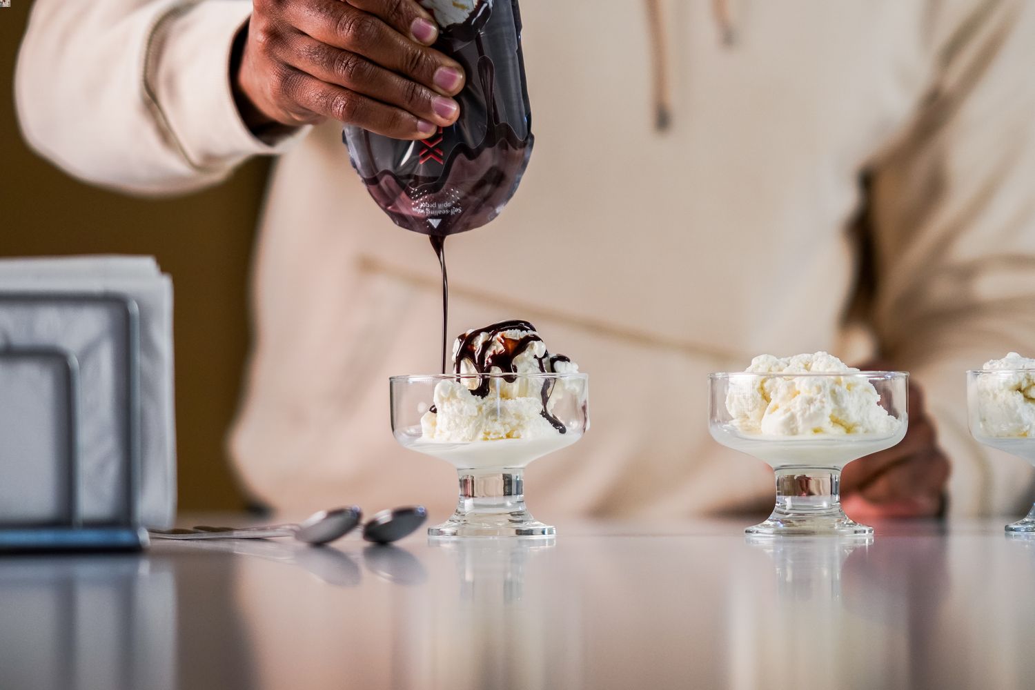 Person squeezing chocolate syrup out of an AeroFlexx Pak onto an ice cream sundae