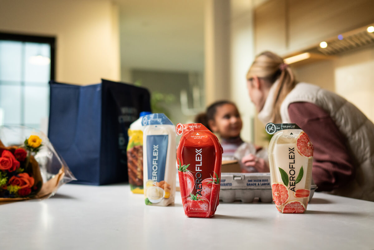 Colorful AeroFlexx packaging and a bouquet on a kitchen counter, with a woman and child in the background.