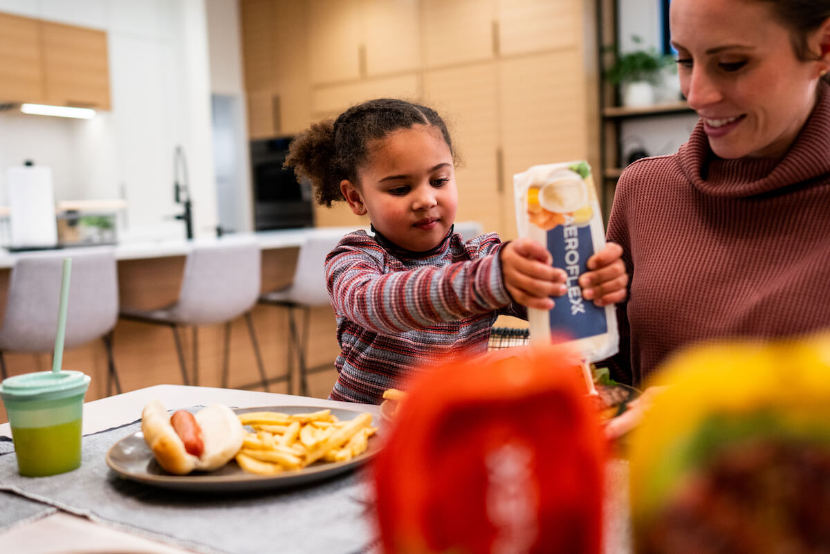 Young girl squeezing condiment out of AeroFlexx Pak onto a burger