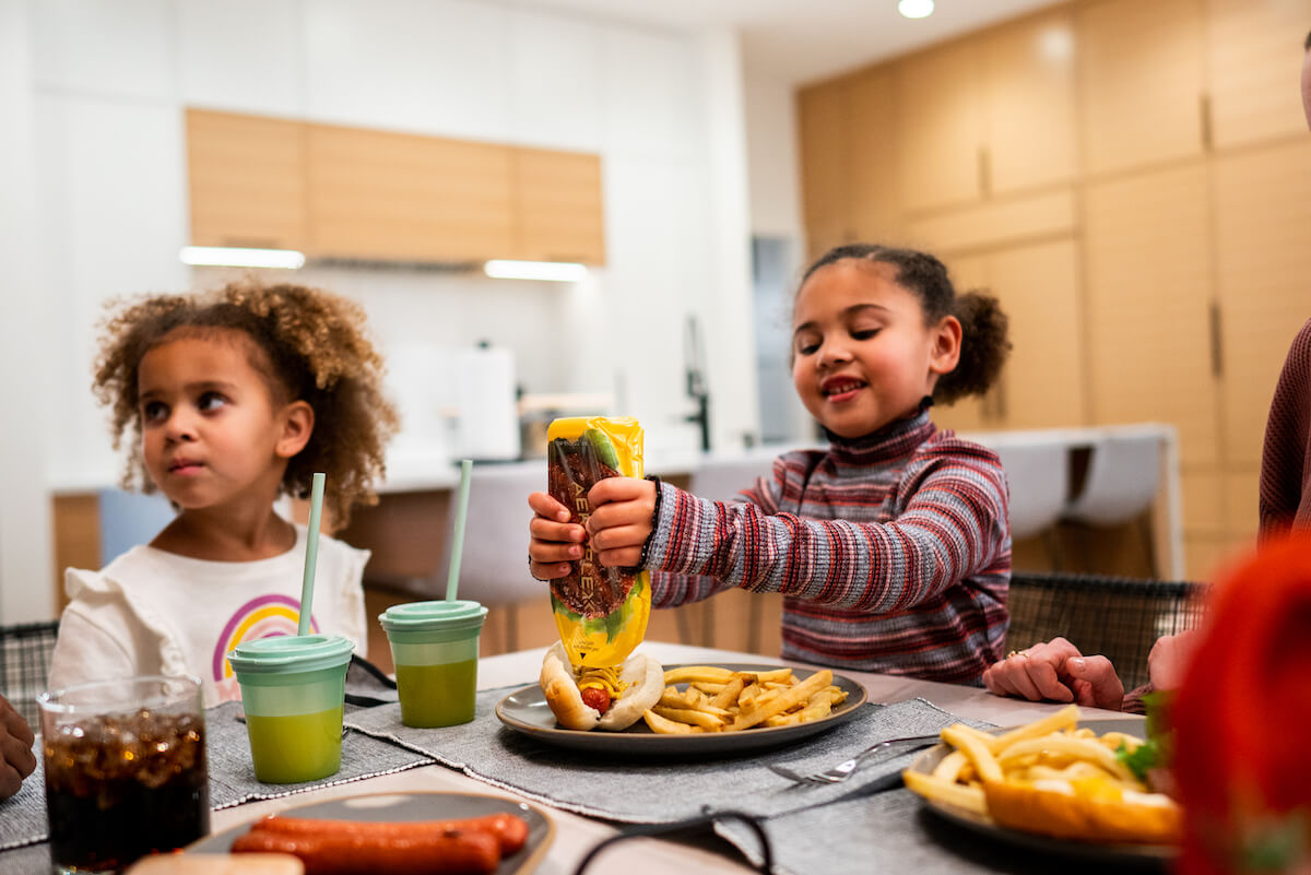 Young girl using Aeroflexx Pak at dinner to squeeze mustard onto a hot dog