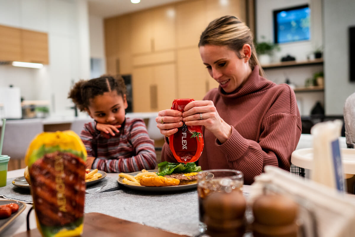 Woman at dinner table squeezing ketchup out of an AeroFlexx Pak onto a burger