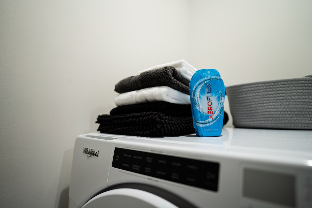 Stacked towels and a AeroFlexx detergent bottle on a washing machine.